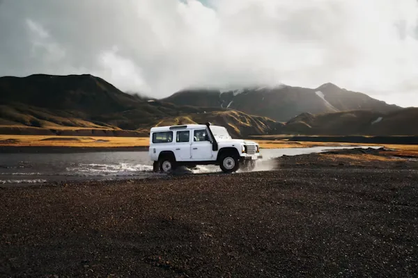 4x4 blanc au bord d'une rivière au pied des montagnes